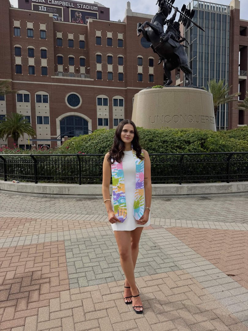 Jessica Harris on the Florida State campus in a white dress and a graduation stole covered in colorful painted handprints